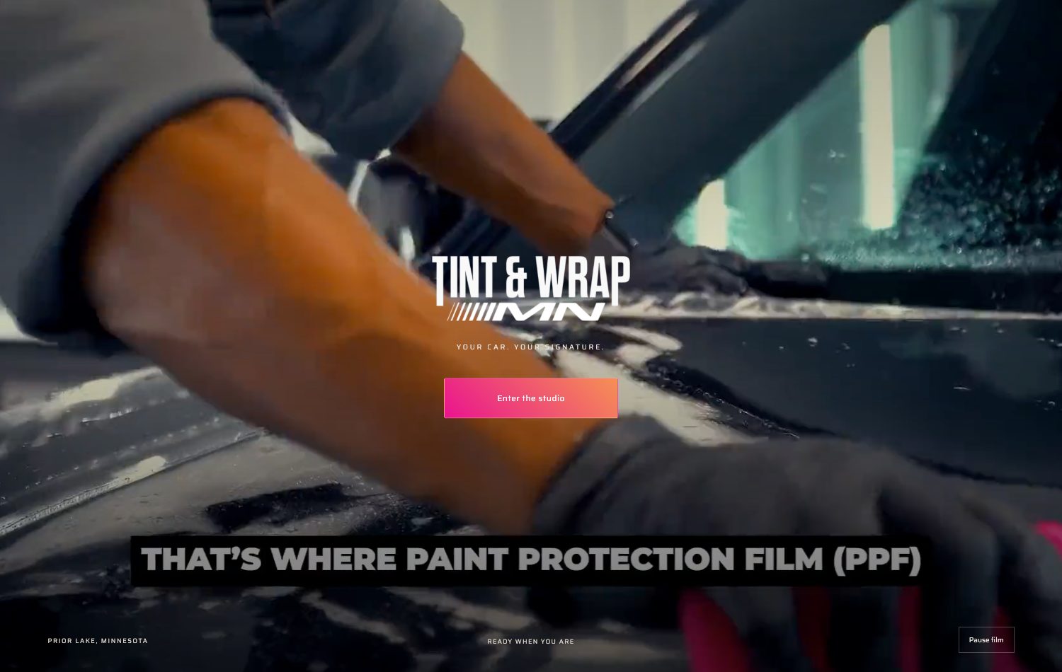 Entrance film: a technician laying film on a dark car, with Enter the studio